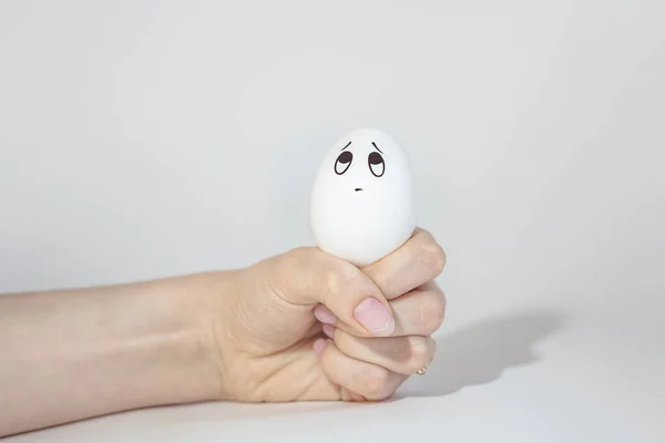 egg with a sad painted face in a fist, looks up, emotions on the egg, white background