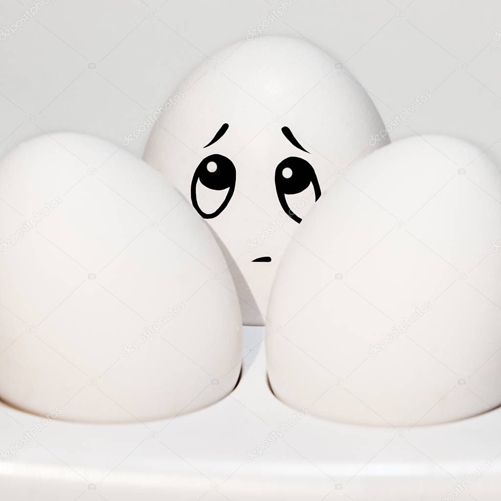 egg with a sad painted face between two white eggs, looks up, emotions on the egg, white background