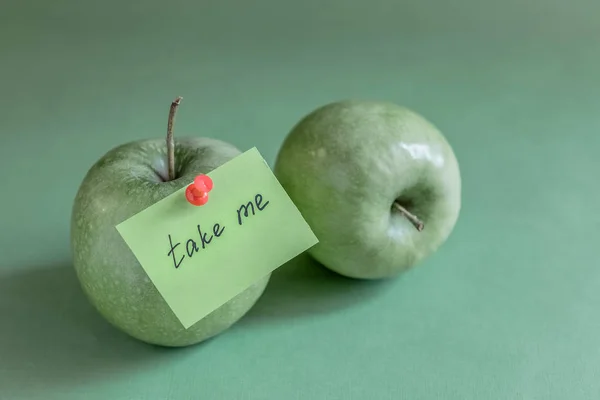 two green apples on green background, note on apple, red pin, take me