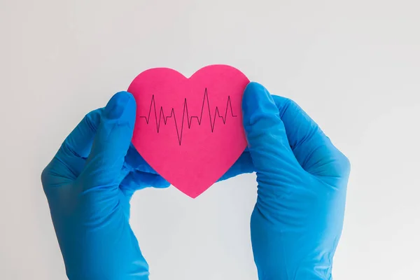 two hands in blue gloves hold a red pink heart, a heart cardiogram, a symbol, doctors protect life and heart, heart disease, white background