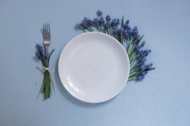 mavi bir arka plan üzerinde masa ayarı, bir kişi için alan, beyaz plaka, mavi çiçekler, çiçekler, bahar masa bir çatal