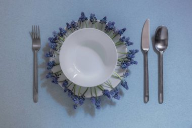 mavi bir arka plan üzerinde masa ayarı, bir kişi için alan, iki beyaz plaka, plaka etrafında mavi çiçekler, çatal, masa yaylar