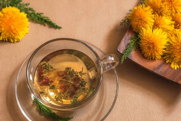 Herbal dandelion tea for health, alternative medicine, yellow dandelion flowers on a plate, green herbs and flowers