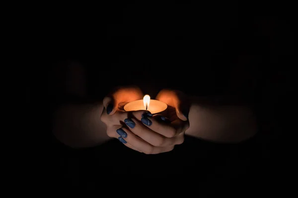 candle in hand, female hands hug the candle, warm living fire, black around