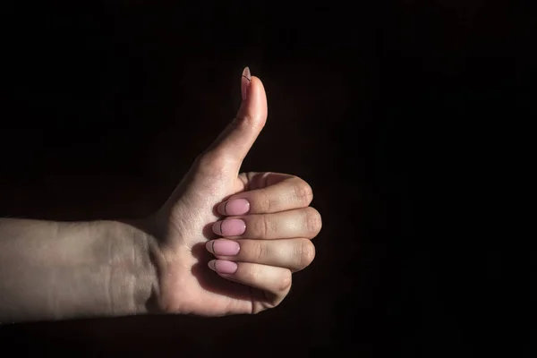good hand sign, thumb up, symbol on a black background, female hand in a positive gesture