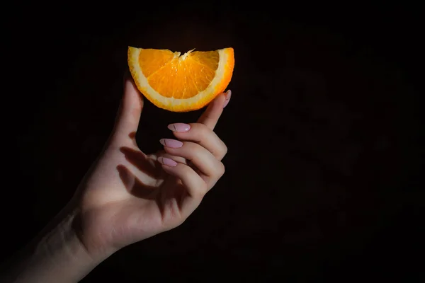 orange slice in female hand, bright orange citrus fruit, hand isolated on black background