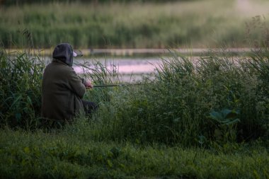 gün doğumunda gölün nehir kıyısında oturan balıkçı, elinde olta, yaşlı adamın hobi