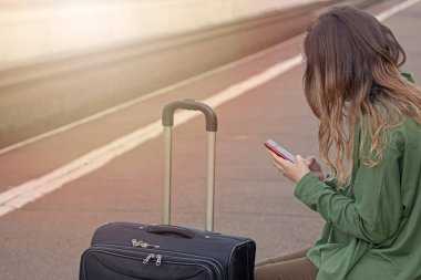 kız platformda oturuyor, treni bekliyor, treni, telefona bakıyor, program, evden ayrılıp, bir bavul.