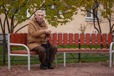 Yaşlı bir adam bankta oturur ve kameraya bakar. Sokaktaki bir emeklinin portresi.