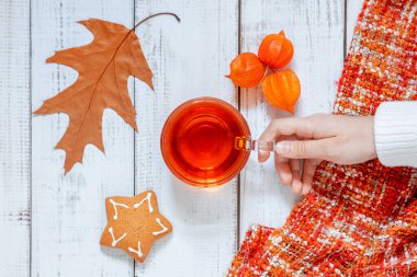 Elleri çay fincanı, masada kuru sonbahar yaprağı, portakal suyu ve kurabiyeler, ev konforu ve bir fincan sıcak çay ile sonbahar havası.