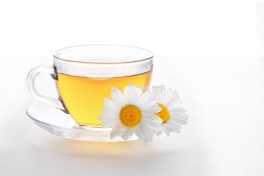 Beyaz arka planda fincan ve çay tabağı, fincanda bitki çayı, çay tabağında iki papatya, doğal şifalı bitkiler, alternatif tıp konsepti