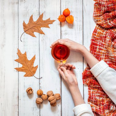 Sonbahar arkaplanı elinde bir fincan çayla ahşap bir masanın üzerinde güzel düşmüş yapraklar, bitki salatası, fındık ve örülmüş bir eşarp, sıcak, rahat bir atmosfer.,