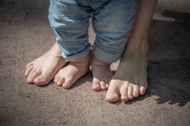 Bebeğin küçük bacakları kumda çıplak ayakla annenin ayaklarının yanında, bebeğin ilk adımları., 