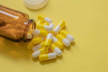Sarı arka planda ilaç kapsülleri, ilaç şişesi, beslenme takviyeleri.