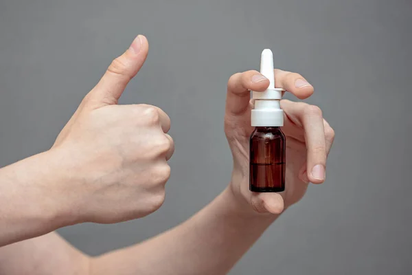 nasal spray in hand, cure for rhinitis, bottle of liquid in hand, thumb up, cold and snot treatment
