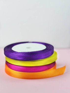 Rulo bir yığın saten renk dikey parlak mavi, mor, sarı ve yeşil kurdela süsleme ve hediye paketleri için pembe bir arka plan üzerinde