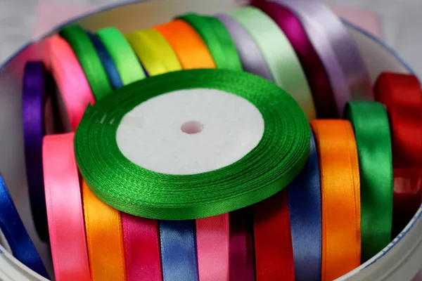 A lot of colored beautiful satin ribbons on top green ribbon top view for decoration, gift wrapping and sewing in a textile store bright and colorful background