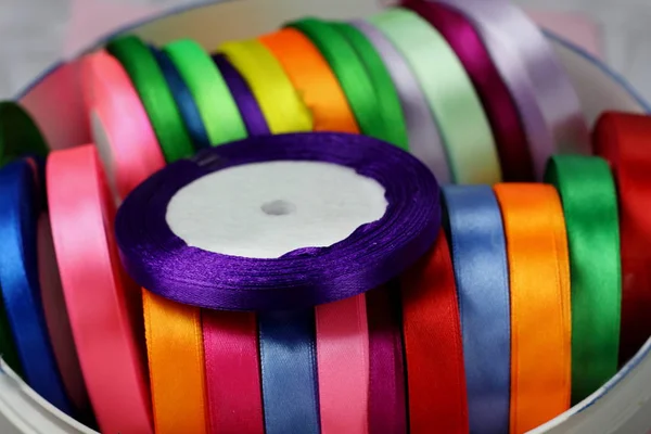 A lot of colored beautiful satin ribbons on top purple ribbon top view for decoration, gift wrapping and sewing in a textile store bright and colorful background