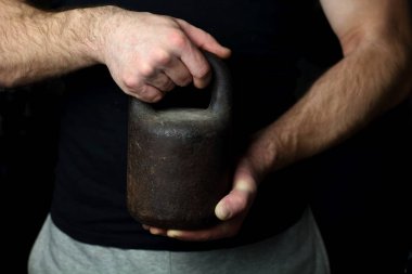 Bir adam siyah bir tişört ve eşofman vintage bir ağırlık vahşice spor, güç, erkeklik, fitness bir sembolü olarak güçlü elinde tutan