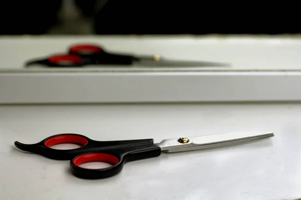 Hairdressing tools scissors for a hairdresser on a white shelf are reflected in the mirror