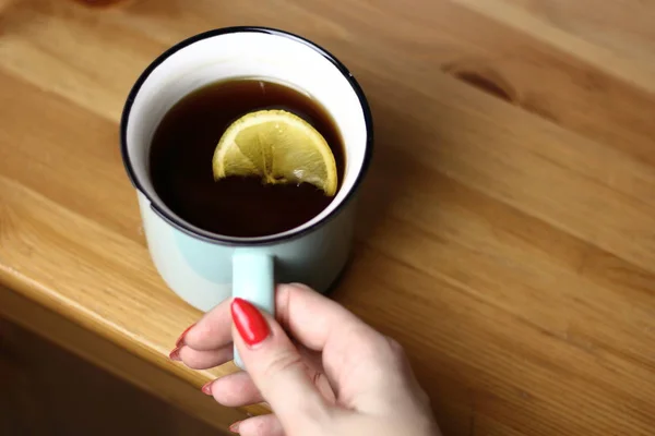 Hot warming tea with lemon in a light blue mug with a brewed tea strainer on a table with a wooden texture