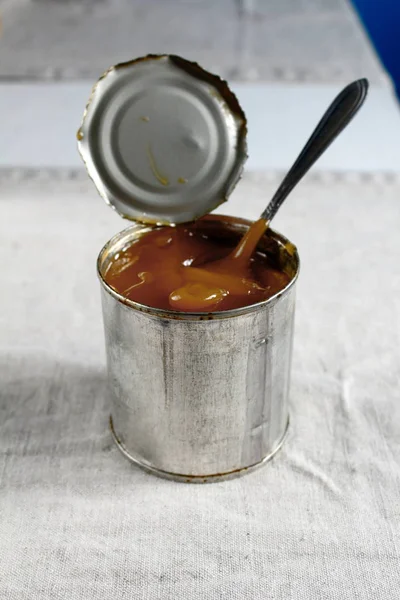 自制的传统煮炼乳从桌子上的勺子里倒出来的铁罐 — 图库照片