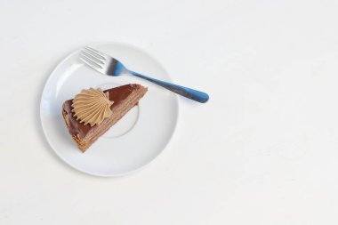 Tatlı çatal üstten görünüm ile beyaz tabakta çikolatalı krem dekorasyonu ile lezzetli çikolatalı kek parçası. Menü stili