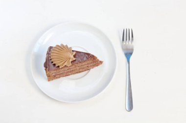 Tatlı çatal üstten görünüm ile beyaz tabakta çikolatalı krem dekorasyonu ile lezzetli çikolatalı kek parçası. Menü stili