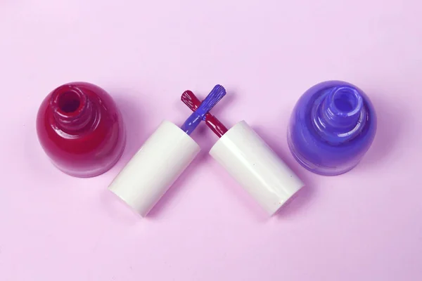 Blue and  red nail lacquer  polish bottles and  crossed nail brushes on pink background. Nail service industry