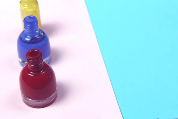 Blue, red, yellow nail lacquer  polish bottles and nail brushes on pink background. Copy space for text. Nail service manicure