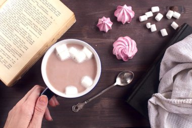 ocoa kahve marshmallow bir kitap yanındaki ahşap bir masa üzerinde bir koyu mavi Kupası ile bir kaşık ve beze üst atmosferik rahat düz lay görüntülemek