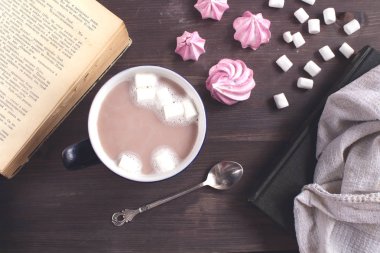 ocoa kahve marshmallow bir kitap yanındaki ahşap bir masa üzerinde bir koyu mavi Kupası ile bir kaşık ve beze üst atmosferik rahat düz lay görüntülemek