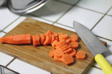 Mutfakta bir bıçakla bir ahşap kesme tahtası üzerinde yemek yemek yemek için havuç dilimlenmiş. Vejeteryan beslenme