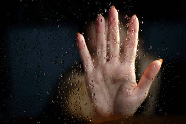 Female hand palm silhouette through behind the window with raindrops reaching for the glass. A request for help, depression, stress blurred bokeh background. Refusal  denial of alcohol and drugs