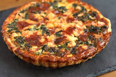 Restoranda siyah bir arduvaz plaka üzerinde peynir, ıspanak ve domates ile fench geleneksel rustik quiche pizza