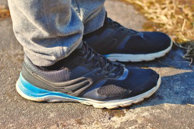 Sağlıklı ve aktif spor yaşam tarzları için asfalt konsepti üzerinde beyaz ve mavi tabanlı gri eşofmanlı bacaklar ve siyah koşu ayakkabıları