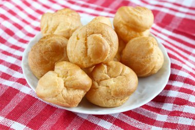 Kırmızı-beyaz kafes içinde rustik bir masa örtüsü ile bir masada çay ve kitap ile beyaz bir fincan yanında muhallebi ile ev yapımı küçük kek profiterole choux pasta