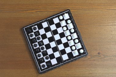 Ahşap bir yüzey üzerinde siyah beyaz satranç ile katlanabilir plastik satranç tahtası. Üstte görüntü