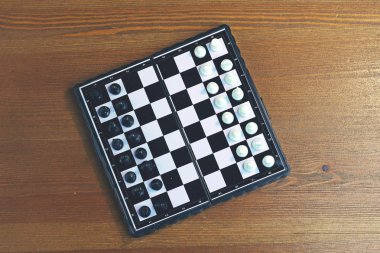 Ahşap bir yüzey üzerinde siyah beyaz satranç ile katlanabilir plastik satranç tahtası. Üstte görüntü