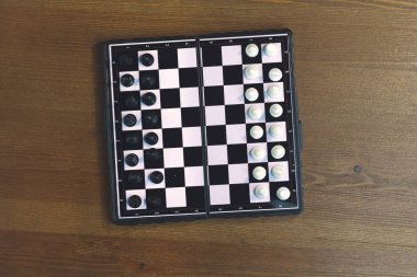 Ahşap bir yüzey üzerinde siyah beyaz satranç ile katlanabilir plastik satranç tahtası. Üstte görüntü