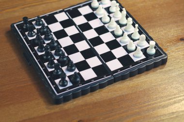 Ahşap bir yüzey üzerinde siyah beyaz satranç ile katlanabilir plastik satranç tahtası. Üstte görüntü