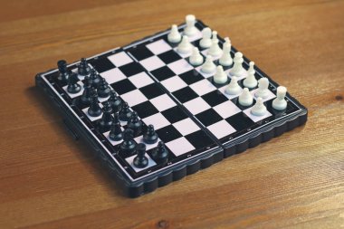 Ahşap bir yüzey üzerinde siyah beyaz satranç ile katlanabilir plastik satranç tahtası. Üstte görüntü