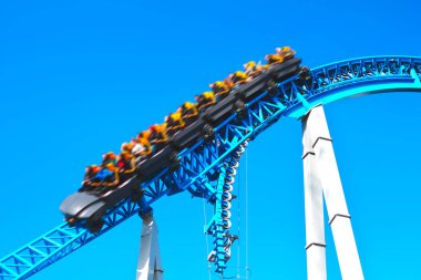 İnsanlar dinlenmek, eğlenmek ve hızlı tatil hafta sonu eğlence parkı döngü ile mavi ürkütücü korkunç roller coaster binmek. Rollercoaster hareket le bulanık