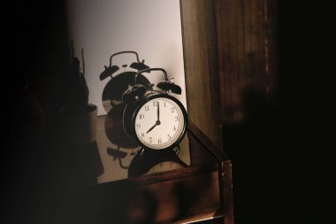 Sert gölgeler ile batan güneşin ışınları nda cilalı bir yüzeyde yansıması ile ahşap bir başucu masada Siyah retro vintage çalar saat