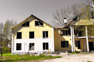 Yangından sonra yanan büyük bir kır evi gri gökyüzüne karşı çökmüş hasarlı çatı ile. gri bir gökyüzüne karşı çökmüş hasarlı çatı ile büyük bir kır evi yandı