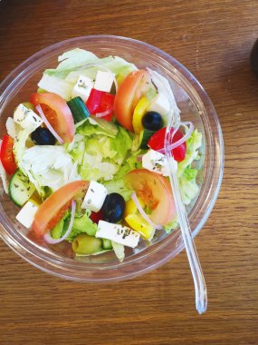 Plastik çatal üst görünümü ile plastik tek kullanımlık bir kapta domates, zeytin, marul, sarı biber ve peynir ile bir kafe götürmek yunan sebze diyet salatası