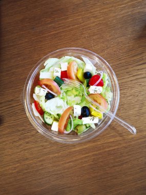 Plastik çatal üst görünümü ile plastik tek kullanımlık bir kapta domates, zeytin, marul, sarı biber ve peynir ile bir kafe götürmek yunan sebze diyet salatası