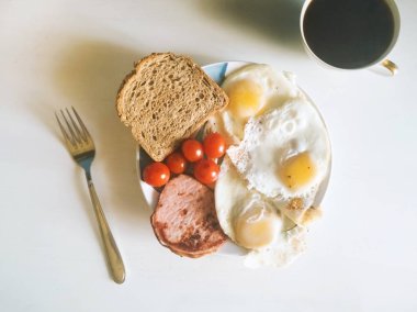 Sağlıklı organik dengeli kahvaltı, doğru beslenme, omlet, yumurta, domates kiraz, kepekli ekmek ve pastırma mavi-beyaz plaka üzerinde çatal ile yakın yatıyor, fincan siyah kahve üst görünümü. Instagram stili