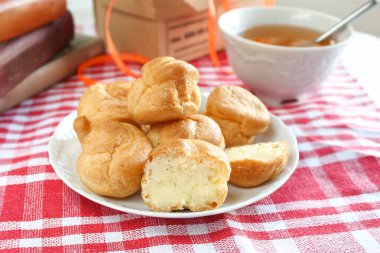 Isırılmış ev yapımı küçük kek karne choux pasta kırmızı-beyaz kafeste rustik bir masa örtüsü ile bir masada çay ve kitap ile beyaz bir fincan yanında muhallebi ile