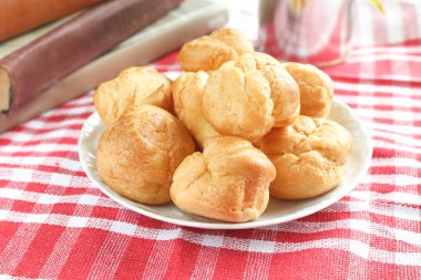 Isırılmış ev yapımı küçük kek karne choux pasta kırmızı-beyaz kafeste rustik bir masa örtüsü ile bir masada çay ve kitap ile beyaz bir fincan yanında muhallebi ile